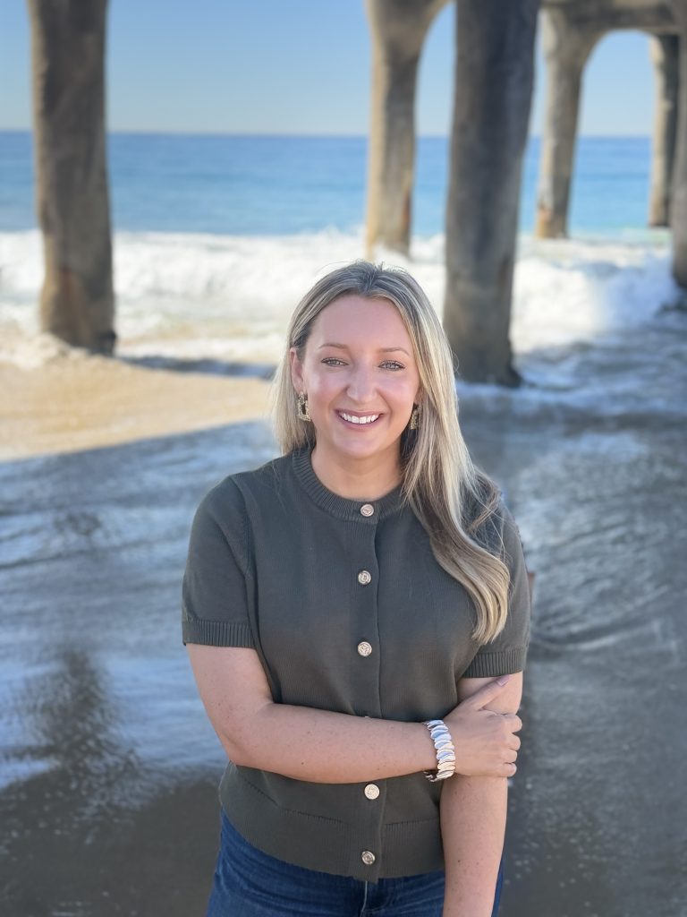 Erin Connelly, BCBA, founder of Coastal Behavior Care, standing on the beach under a pier