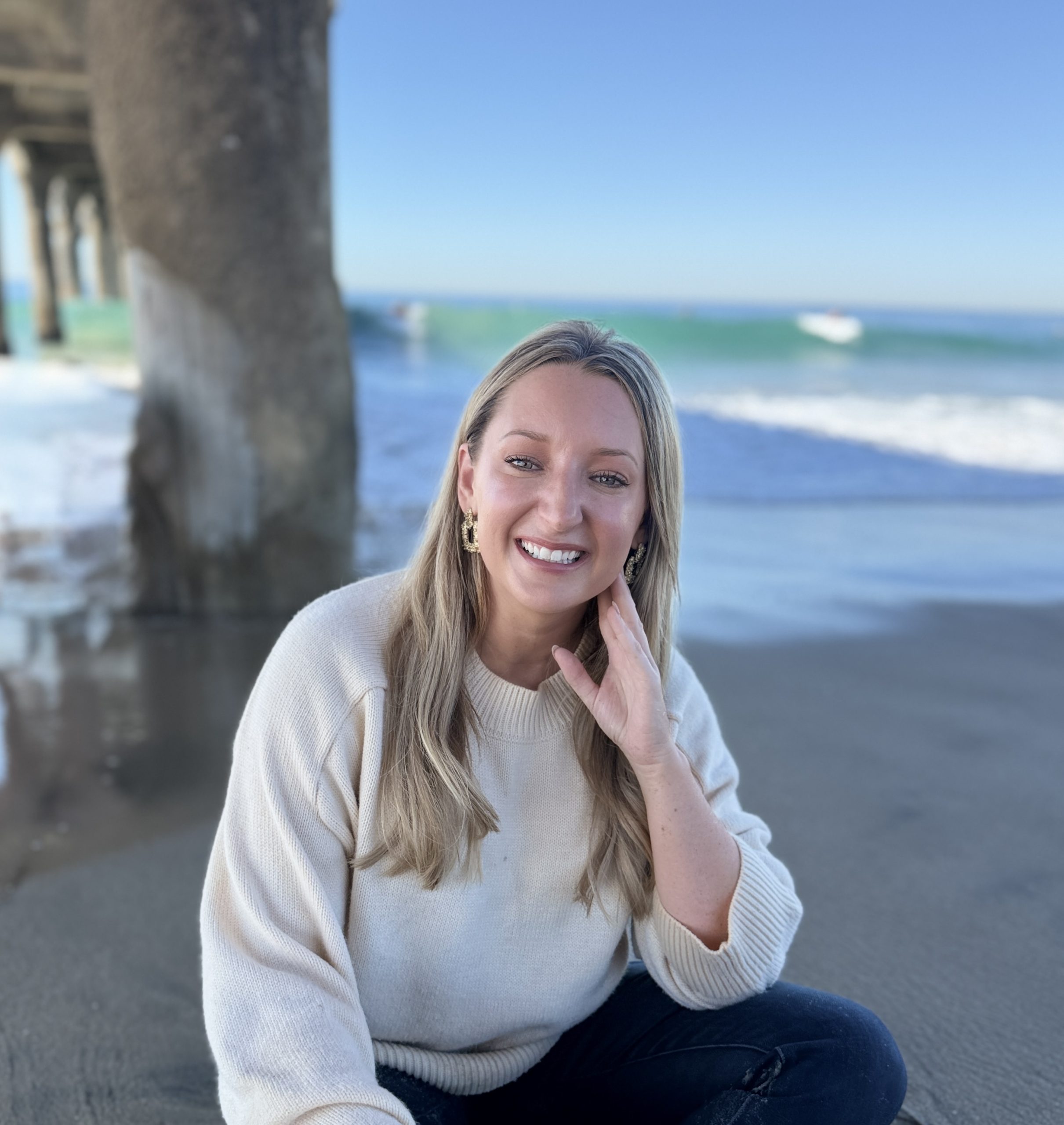 Erin Connelly, BCBA, founder of Coastal Behavior Care, sitting on the sand under a pier